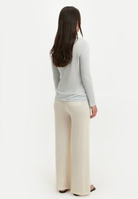 Hellblaues Langarmshirt mit Rundhalsausschnitt und weicher Textur, kombiniert mit cremefarbenen Hosen mit weitem Bein und einer kleinen Taschenapplikation.