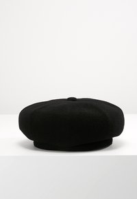 Berretto di lana nera con un piccolo bottone superiore, posato su una superficie bianca contro uno sfondo grigio chiaro uniforme.