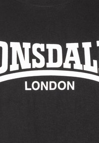 Zwarte katoenen T-shirt met opvallende witte tekst in een boogontwerp met "LONSDALE" en "LONDON". Zachte textuur, ronde hals, casual pasvorm.