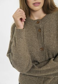 Hnědý pletený cardigan s texturovaným povrchem, vybavený třemi dřevěnými knoflíky, žebrovaným límcem a manžetami a jemnými třpytivými akcenty.