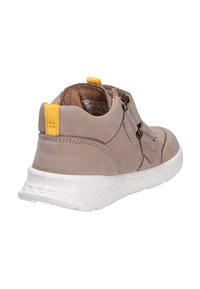 Baskets pour tout-petit marron clair avec semelle blanche texturée, languette de traction jaune au talon et fermetures à sangle latérales, vues sous un angle arrière.