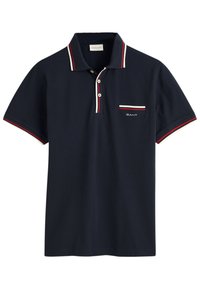 Polo shirt azul marino de algodón con una tapeta de tres botones, un cuello de rayas rojo y blanco en contraste, y un pequeño bolsillo a rayas.