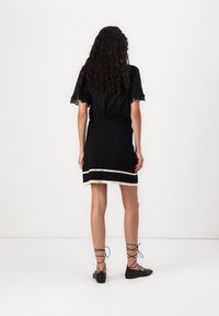 Black blouse with lace trim, gathered waist, and a black pleated skirt featuring a cream band at the hem. Flat black lace-up shoes.