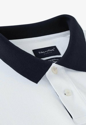Chemise polo blanche avec un col marine, dotée d'une patte de boutonnage à deux boutons et d'un tissu texturé. L'étiquette indique "Eden Park Paris."