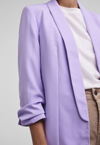 Lavendelfärgad blazer i ett lätt tyg, med sjalkrage, uppvikt ärmar och en skräddarsydd passform. Bärs över en vit t-shirt.