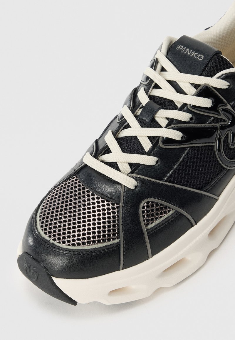 Czarne sneakersy wykonane z siateczki i skóry, z białymi sznurówkami, masywną kremową podeszwą oraz logo na języku i pięcie.