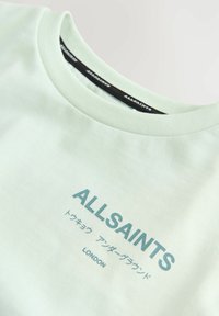 Šviesiai mėtinės spalvos marškinėliai su apvaliu kaklu, papuošti tamsiai žaliai mėlynu logotipu ir tekstu. Pagaminti iš minkštos medvilnės audinio su lygiu paviršiumi.