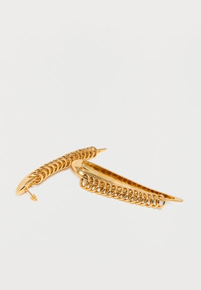 Ζευγάρι λαμπερών χρυσών κλιπ για τα μαλλιά με λεπτομέρειες από συστρεφόμενο σύρμα κατά μήκος των καμπυλωτών άκρων τους σε λευκό φόντο.