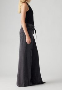 Spodnie dżinsowe czarne, wysoko w pasie, o szerokich nogawkach, z paskiem wiązanym, z delikatnymi szwami i okrągłymi tylnymi kieszeniami. Gładka tekstura.