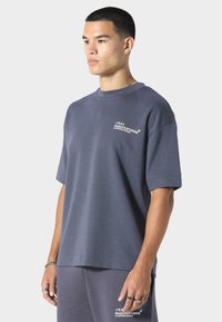 Szara krótka bluza z rękawem, o luźnym kroju, z wyraźnym białym napisem i gładką fakturą materiału, w komplecie ze spodniami w tym samym kolorze.