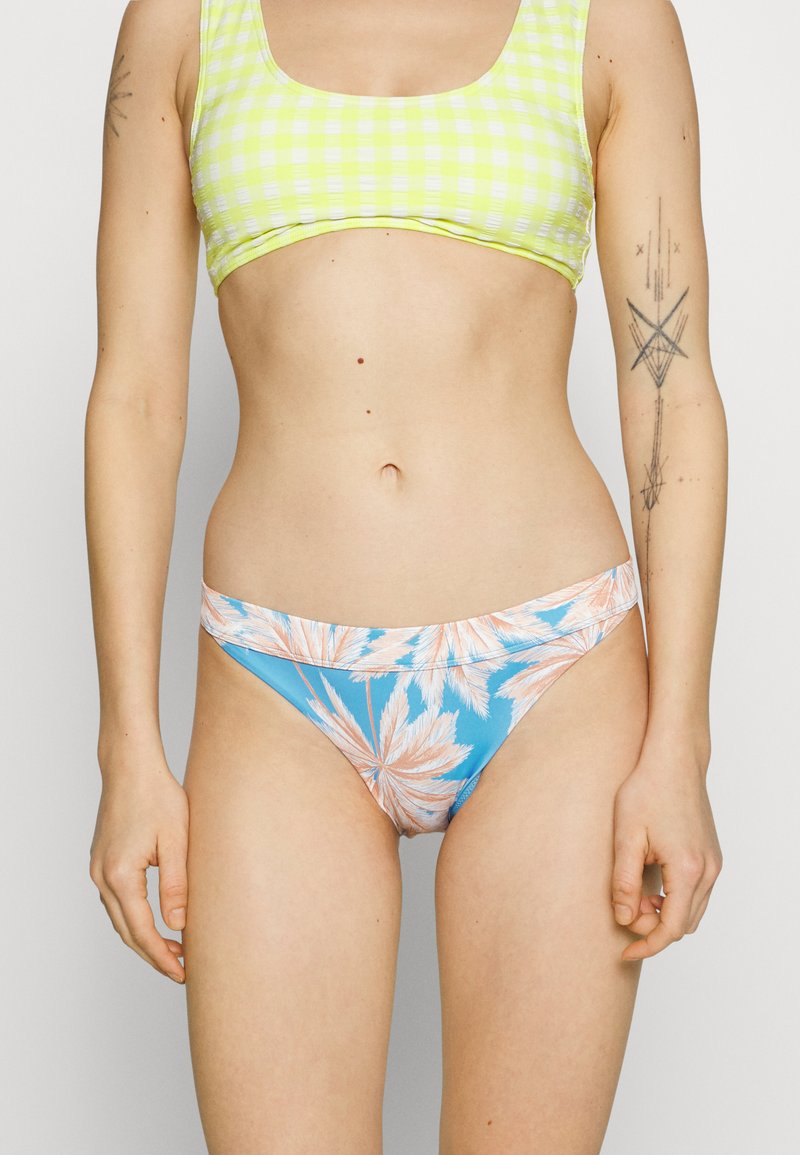 Σετ μπικίνι με κίτρινο καρό crop top και μπλε κάτω μέρος με εκτυπώσεις φύλλων φοίνικα. Το υλικό φαίνεται ελαστικό, το σχέδιο είναι σπορ και ζωντανό.