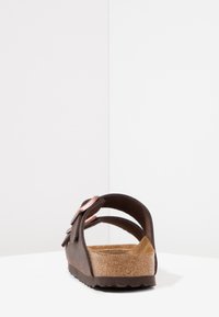 Brun bakvy av en sandal med korkfotbädd, smala läderremmar och en koppardetalj. Texturerad sula. Minimalistisk design.