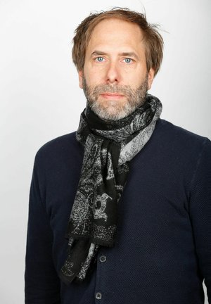 Schal mit schwarz-grauem Muster aus weichem Stoff, stilvoll um den Hals gewickelt, mit Fransen. Über einem marineblauen Pullover getragen.