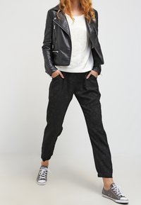 Zwarte met een patroon gestreepte broek en een wit sweatshirt met een logo, gecombineerd met een cropped zwart leren jack en grijze sneakers.