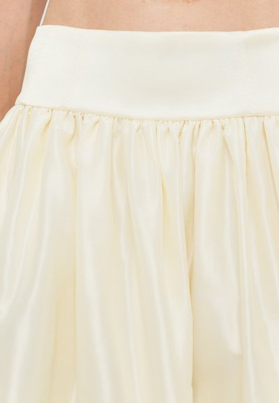 Falda de color crema con un diseño acampanado y plisado, hecha de una tela suave y ligera. Presenta una cinturilla ancha y suave.