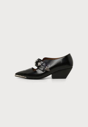 Black pointed-toe leather shoe with low angled heel, decorative silver studs, and a strap across the top.