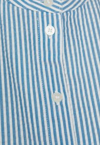 Chemise à rayures bleues et blanches avec un devant boutonné, des boutons blancs et un tissu texturé. Les rayures sont régulièrement espacées et étroites.