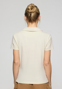 Krämfärgad polo tröja med klassisk krage, korta ärmar och rak nederkant. Slät textur och minimalistiska designdetaljer.