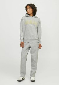 Sudadera gris con "SOCIAL CLUB" impreso en amarillo en la parte frontal, combinada con pantalones de chándal grises a juego. Ambos están hechos de un material suave.