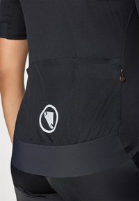 Schwarzes Fahrradtrikot aus strukturiertem Stoff, mit kurzen Ärmeln und einer gepolsterten Tasche. Auffälliges Logo in Weiß auf der Rückseite.