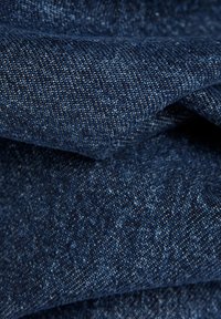 Țesătură din denim de culoare albastru închis, cu o suprafață texturată. Împletitura este strânsă, cu scoici deschise, creând adâncime și interes vizual.