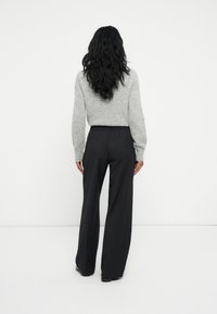 Grijze gebreide trui met lange mouwen, gecombineerd met zwarte wijdvallende broek met een elastische tailleband, gezien van achteren.