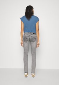 Jeans ajustados grises con dos bolsillos traseros y costuras blancas, combinados con una blusa azul de manga corta. Los jeans presentan un corte ajustado y piernas estrechas.