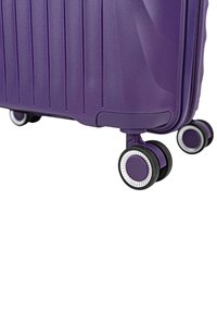 Maleta dura morada con estrías verticales, equipada con cuatro ruedas multidireccionales y bordes con acentos plateados. Textura suave.