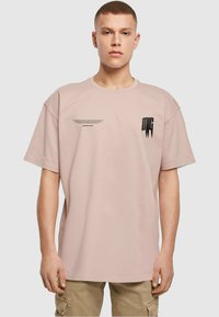 Lyserød bomulds T-shirt med en afslappet pasform. Har sort grafisk tekst og logoer på fronten. Korte ærmer og rund halsudskæring.