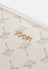 Portefeuille en cuir beige avec des motifs de feuilles en relief et un logo doré "JOOP!". Surface texturée et détail de fermeture éclair doré contrastant.