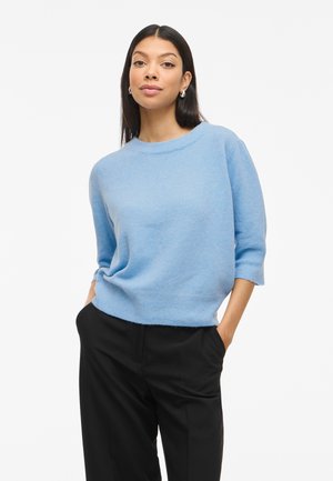 Maglione in maglia blu chiaro con un ampio scollo e design cropped, caratterizzato da maniche a tre quarti e orlo a coste, abbinato a pantaloni neri.
