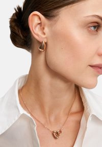 Goldfarbene Ohrringe mit einer abstrakten Tropfenform und einer passenden roségoldenen Halskette mit miteinander verbundenen Herzen.