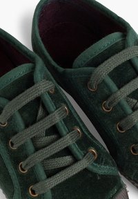 Zelené sametové tenisky s kulatými tkaničkami, bronzovými Řezy a texturovaným povrchem. Interiér je podšitý tmavě fialovou látkou.