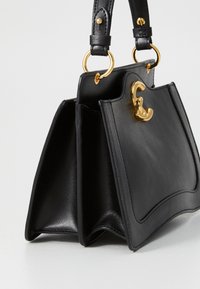 Black leather handbag with a structured shape, featuring a gold-tone hardware clasp and two short handles, smooth texture with minimalistic design.