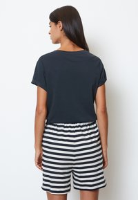 Marinblå kortärmad topp kombinerad med svartvita randiga shorts. Shorts har en elastisk midja och en mjuk tygstruktur.