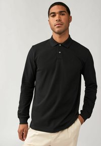 Zwarte polo met lange mouwen, een klassieke kraag, een placket met drie knopen en subtiele logo-geborduurde op de borst. Glad stofoppervlak.