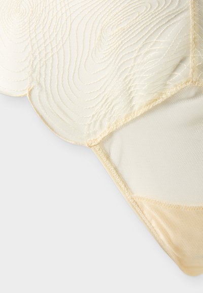 Tissu transparent de couleur crème avec des motifs de couture géométriques et tourbillonnants sur un matériau en maille délicate.