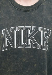 Tmav zelené bavlnené tričko s veľkými bielymi nápismi "NIKE" so zvýrazneným prešívaním. Látka má textúrovaný, opotrebovaný vzhľad.