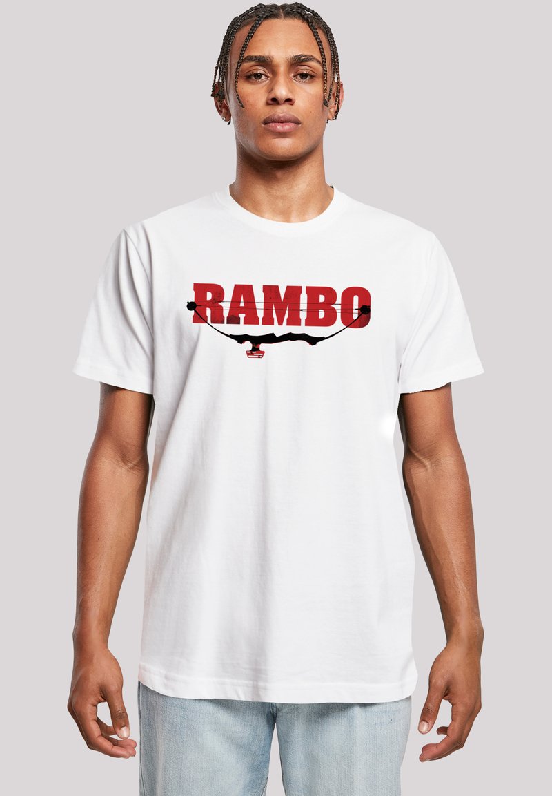White cotton t-shirt featuring a large red "RAMBO" graphic with a black silhouette and design elements. Short sleeves and relaxed fit.