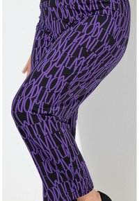 Fioletowe legginsy z powtarzającym się, wyraźnym wzorem tekstu "MODERN" na czarnym tle, wykonane z elastycznego materiału, o dopasowanym kroju.