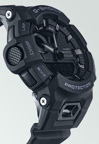 Montre G-Shock noire avec un affichage numérique, un bracelet en caoutchouc texturé, plusieurs boutons et un boîtier de protection avec des accents prononcés.