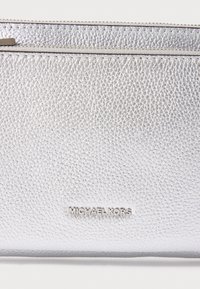 Hopeakosketusnahkainen clutch, jossa on teksturoitu pinta, tyylikäs muotoilu ja hopealla varustettu, kohokuvioitu "MICHAEL KORS" -logo.