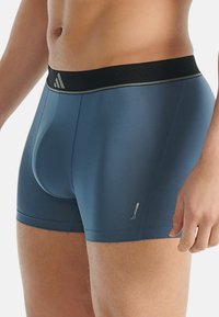 Blå atletiska boxershorts med svart elastisk midja, med en mjuk textur och logotypaccent på underbenet.