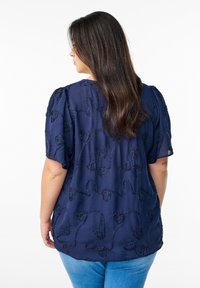 Blusa blu navy con un motivo di ricamo floreale testurizzato, maniche corte a sbuffo e vestibilità comoda, abbinata a jeans blu chiaro.