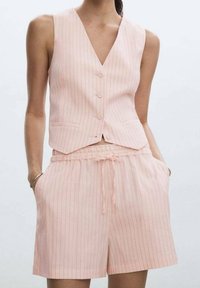 Gilet sans manches rose clair avec des rayures blanches verticales et trois boutons ; associé à un short assorti avec taille élastique et poches.