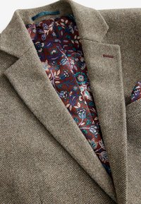 Tweed blazer in brown herringbone pattern, featuring a colorful floral lining and a pocket square in complementary colors.