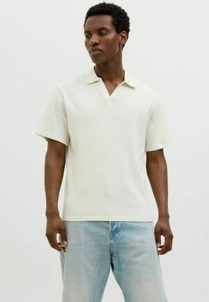 Lichtbeige geribbelde poloshirt met een V-hals en korte mouwen, gecombineerd met lichtblauwe spijkerbroek. Heeft een zachte textuur en subtiele glans.