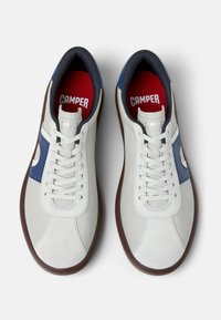 Zapatillas de cuero blanco con detalles en azul y suela de goma marrón. Características de diseño con cordones y cuello acolchado en color azul marino. Plantilla roja visible.