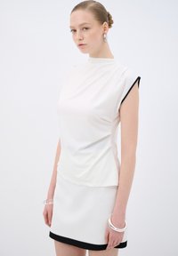 Top bianco a maniche corte con scollatura alta, caratterizzato da dettagli neri alle maniche. Abbinato a una mini gonna bianca con orlo nero.