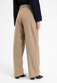 Beige wijde broek met een gladde textuur, hoge tailleband en zijzakken, gecombineerd met zwarte schoenen met blokhakken.